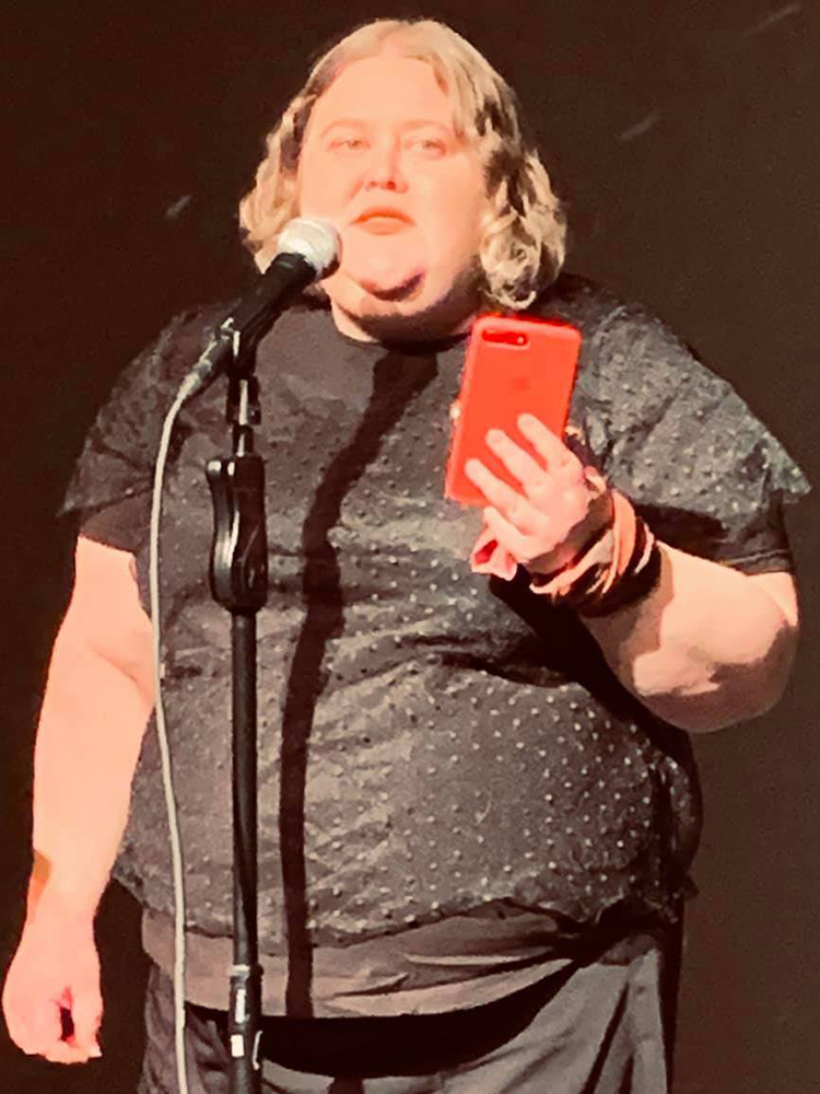 Alison Bergblom Johnson, a plus-sized woman with curly blonde hair, wearing black while holding a red cell phone